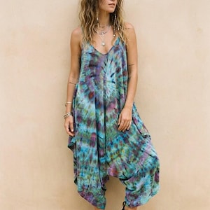 May include: A tie-dye jumpsuit in blue, purple, and green. The jumpsuit has a V-neck, wide legs, and a relaxed fit. Black sandals complete the look. The garment is made of a soft, flowing fabric. The model is wearing black sandals.