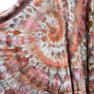 Op de afbeelding: Een mouwloos hemdje met een spiraalvormig tie-dye patroon in tinten terracotta, oudroze, gedempt bruin en cr&egrave;me. Het kledingstuk heeft een ronde halslijn en een los, vloeiend silhouet met zichtbare stiksels langs de rand van de kraag.