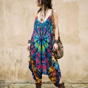 Könnte beinhalten: Ein ärmelloser Jumpsuit mit einem lebendigen Batikmuster in Blau-, Rot-, Gelb- und Grüntönen. Das Kleidungsstück hat einen tiefen V-Ausschnitt, eine lockere Passform mit tiefem Schritt und wird mit braunen Schnürstiefeln aus Leder kombiniert.