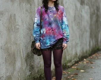 May include: A long-sleeve crewneck sweatshirt featuring a vibrant galaxy print in shades of purple, blue, and pink with scattered white star patterns. The sweatshirt is paired with black distressed denim shorts, dark purple ribbed tights, and black boots.