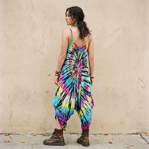 May include: A sleeveless jumpsuit featuring a vibrant tie-dye pattern in shades of blue, yellow, pink, and black. The garment has thin spaghetti straps, a low-cut back, and a loose, drop-crotch silhouette that tapers toward the lower leg area.