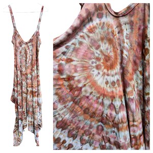 Op de afbeelding: Een mouwloze jurk met een spiraalvormig tie-dye patroon in tinten terracotta, oudroze, bruin en cr&egrave;me. Het kledingstuk heeft een diepe ronde halslijn, dunne schouderbandjes en een asymmetrische zoom met meerdere overlappende panelen.