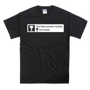 May include: Black t-shirt with a white graphic that says "You have earned a trophy Got Dressed" with a trophy icon.
