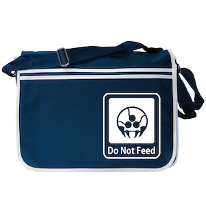 Peut inclure: Un sac à bandoulière en toile bleu avec une bordure blanche et un patch carré blanc représentant un envahisseur spatial noir et blanc avec le texte "Do Not Feed".