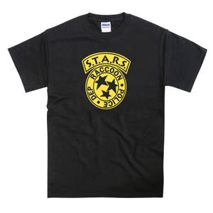May include: Black t-shirt featuring a yellow S.T.A.R.S. logo. The logo displays the words "S.T.A.R.S." and "Raccoon City Police Department" surrounding three stars.