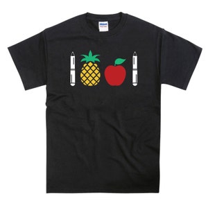 Op de afbeelding: Zwart T-shirt met een ananas, een appel en twee pennen bedrukt op de voorkant.