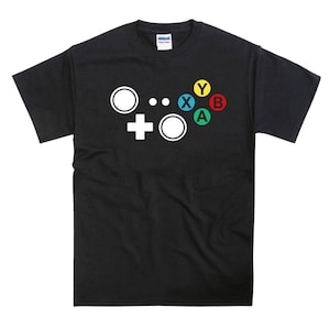 May include: Black t-shirt with a white graphic of a video game controller. The controller has four colored buttons: yellow, red, green, and blue. The buttons are labeled "Y", "B", "A", and "X".