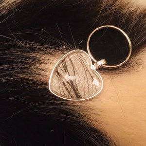 May include: A silver heart-shaped keychain with a clear resin insert containing black hair strands and glitter.