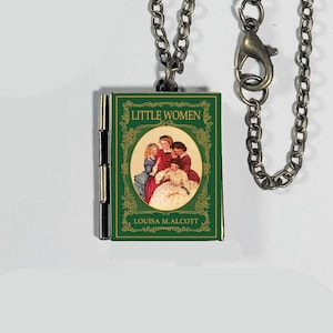 May include: A miniature book pendant necklace featuring the cover of "Little Women" by Louisa M. Alcott. The green book cover has an oval illustration of four women. The pendant hangs from a silver-colored chain.