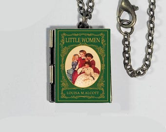 May include: A miniature book pendant necklace featuring the cover of "Little Women" by Louisa M. Alcott. The green book cover has an oval illustration of four women. The pendant hangs from a silver-colored chain.