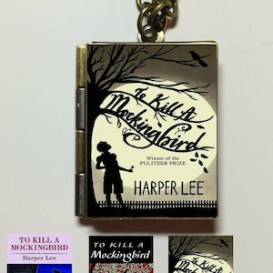May include: A silver locket necklace with a black and white image of a tree, a bird, and a child. The locket has the text "To Kill a Mockingbird" and "Harper Lee" on it. The locket is surrounded by a gold chain.
