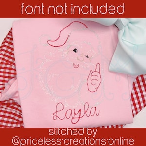 May include: Pink embroidered shirt with a cartoon Santa Claus design and the name "Layla" stitched in red thread. The shirt is stitched by "priceless creations online".
