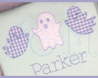 Peut inclure: Un fond bleu clair avec trois appliques de fantômes en vichy blanc et bleu. Les fantômes ont des yeux et une bouche brodés. Le nom "Parker" est brodé en fil bleu sous les fantômes.