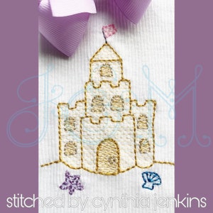 May include: A gold embroidered sandcastle with a pink flag on top. The sandcastle is surrounded by a purple starfish and a white seashell.