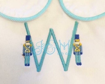 May include: A white embroidered fabric with a blue and white letter W and two blue toy soldier figures on either side of the letter.