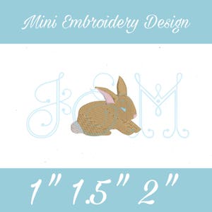 Peut inclure: Miniature de broderie représentant un lapin brun avec des yeux bleus et un nez rose, assis entre les lettres "J" et "M" en écriture cursive bleu clair. Le motif est disponible en trois tailles : 1 pouce, 1,5 pouce et 2 pouces.