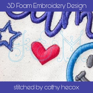 Puede incluir: Primer plano de un diseño de bordado en espuma 3D que presenta la palabra "Dream" en hilo azul, un corazón rojo, una estrella azul y un diseño azul y gris. El texto "stitched by cathy hecox" está en la parte inferior de la imagen.