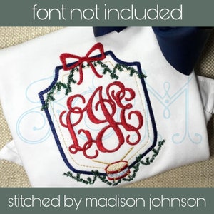 Puede incluir: Una camisa blanca con un monograma bordado en rojo, verde y dorado en forma de escudo con un lazo y un tambor. El texto "stitched by madison johnson" está en la parte inferior de la imagen.