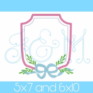 Könnte beinhalten: Rosa und blaues gesticktes Monogramm mit Schleife und Blättern. Das Monogramm hat die Form eines Schildes und die Buchstaben sind "J & M". Das Design ist in den Größen 5x7 und 6x10 erhältlich.