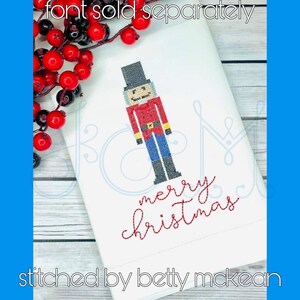 May include: White fabric with a red and blue embroidered nutcracker and the text "merry christmas" in red thread.