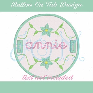 Op de afbeelding: Een rond, wit borduurmotief met een groene rand. Het ontwerp heeft een bloemenpatroon met twee blauwe bloemen en groene ranken. Het woord "Jamie" is in roze cursieve letters in de cirkel geschreven.