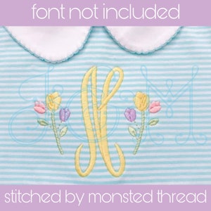 May include: A light blue and white striped fabric with a yellow embroidered letter "L" and yellow embroidered flowers with pink, purple, and yellow accents. The text "stitched by monsted thread" is at the bottom of the image.