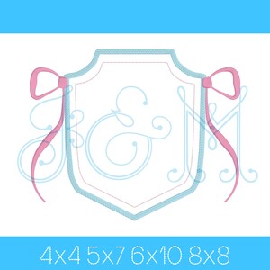 Puede incluir: Un diseño de bordado de monograma con las letras "J & M" en una fuente de escritura azul dentro de un escudo azul y blanco con lazos rosas a cada lado. El diseño está disponible en los tamaños 4x4, 5x7, 6x10 y 8x8.