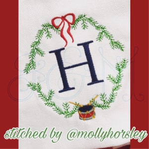 Könnte beinhalten: Gestickte Weihnachtsgirlande mit einem dunkelblauen Buchstaben H in der Mitte, einer roten Schleife oben und einer roten und goldenen Trommel mit Schlagstöcken unten. Der Text "stitched by @mollyhorsley" befindet sich unten im Bild.
