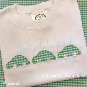 May include: A white t-shirt with a green and blue gingham pattern car applique. The car has two white buttons for wheels. The shirt has the text "Stitched by Kara Boles" on the bottom.