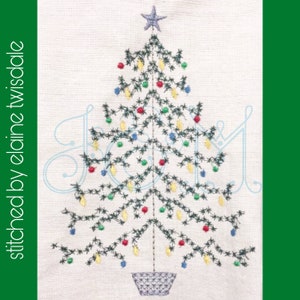 Könnte beinhalten: Ein besticktes weißes Küchentuch mit einem grünen Weihnachtsbaum, der mit roten, gelben und blauen Kugeln und einem Stern verziert ist. Das Wort "Freude" ist in blauer Kursivschrift um den Baum gestickt.