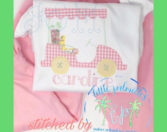 May include: A white onesie with a pink and white gingham golf cart design and the name "caroline" embroidered in white. The onesie is paired with a pink skirt. The image also includes the text "little palmetto" and "stitched by custom embroidery & applique".