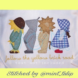 May include: Embroidered design of the Wizard of Oz characters: Scarecrow, Tin Man, Lion, and Dorothy. The characters are standing in a line and the text "follow the yellow brick road" is below them.