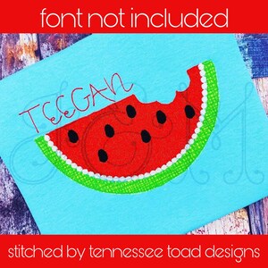 May include: A blue fabric with a red and green watermelon design and the name "TEGAN" embroidered in white thread.