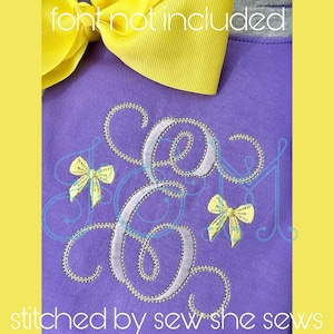 Puede incluir: Una camisa morada con un monograma bordado en plata y lazos amarillos. El texto "font not included" y "stitched by sew she sews" es visible.