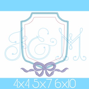 Könnte beinhalten: Ein blaues und weißes Monogramm-Stickmuster mit einer blauen Schleife. Das Monogramm ist "J&M" und das Design hat die Form eines Schildes. Das Design ist in den Größen 4x4, 5x7 und 6x10 erhältlich.