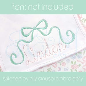 May include: Embroidered design of the name "Linden" in pink thread with a green ribbon bow above it. The design is stitched on a white fabric background.