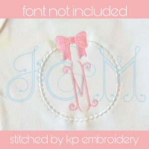 Könnte beinhalten: Ein weißer Stoff mit einem gestickten Monogramm in Rosa in einem Kreis aus weißen Perlen. Das Monogramm ist der Buchstabe "M" mit einer rosa Schleife darüber. Der Text "stitched by kp embroidery" befindet sich am unteren Rand des Bildes.