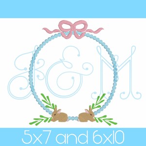 May include: Embroidered monogram design featuring the letters "K & M" in a light blue script font, surrounded by a light blue beaded wreath with a pink bow at the top. Two brown bunnies are nestled in green leaves at the bottom of the wreath. The text "5x7 and 6x10" is written below the wreath.