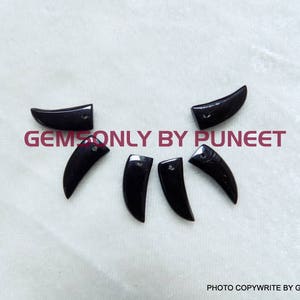 May include: Six black onyx gemstone cabochons shaped like a tooth or fang.  The gemstones are polished and have a smooth, shiny surface.  The cabochons are approximately 1 inch long.  Gems Only By Puneet.