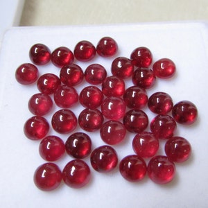 Op de afbeelding: Een verzameling van 30 ronde, rode robijn cabochons. De cabochons zijn glad en gepolijst, met een glanzende afwerking.