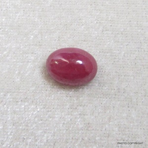 May include: A deep red oval-shaped gemstone with a smooth, polished surface.