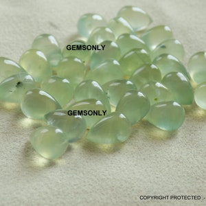 May include: A collection of translucent, pale green gemstones in various shapes, including teardrops and rounded forms. The gems are scattered across a neutral-toned surface, with the text "GEMSONLY" visible in the image.