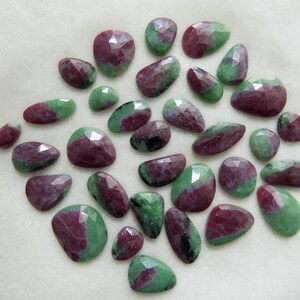 Puede incluir: Una colección de 25 cabujones de piedras preciosas verdes y rosas. Las piedras están facetadas y tienen una variedad de formas y tamaños.