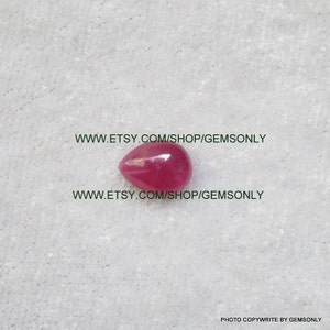Può includere: Una pietra preziosa rosa a forma di lacrima con una superficie liscia e lucida. La pietra preziosa è posizionata su uno sfondo bianco.