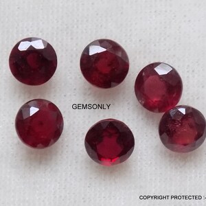 Könnte beinhalten: Sechs runde, rote Edelsteine mit facettierten Kanten. Die Edelsteine sind in einem Halbkreis auf einer weißen Oberfläche angeordnet. Der Text "GEMSONLY" ist im Bild sichtbar.