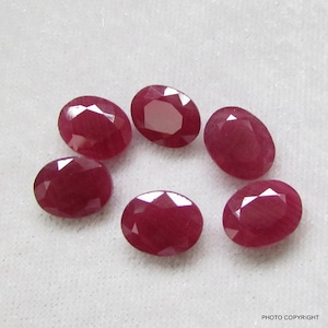 May include: Six oval-shaped, red gemstones. The gemstones are smooth and polished.