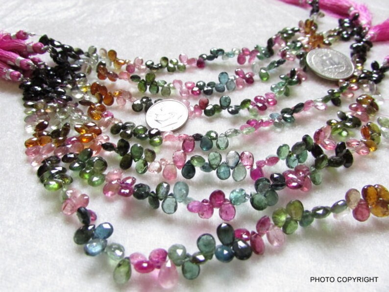 May include: A strand of multi-colored gemstone beads, including pink, green, blue, and brown, in a teardrop shape. The beads are strung on a thin cord and are approximately 5mm in size.
