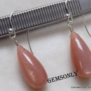 May include: A pair of silver earrings with teardrop-shaped sunstone gemstones. The stones are a light peach color with gold flecks.