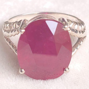 Peut inclure: Une bague en argent ornée d'une grande pierre précieuse rose foncé de taille ovale, maintenue par quatre griffes. L'anneau présente un motif texturé en forme de corde torsadée qui s'étend depuis le sertissage, offrant une finition métallique.