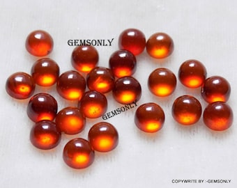 May include: A collection of 20 round, smooth, polished, orange-red gemstones. The gemstones are arranged in a random pattern on a white surface.  The text "GEMSONLY" appears twice in the image.